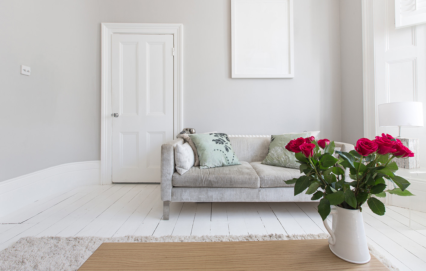 Weiße Zimmertür in einem Wohnzimmer mit einer hellen Couch und Rosen auf dem Tisch.